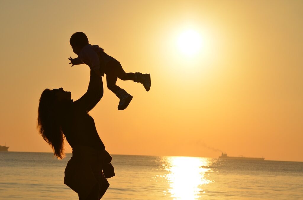 Foto einer Frau, die ihr Kind in die Luft hebt vor einer untergehenden Sonne